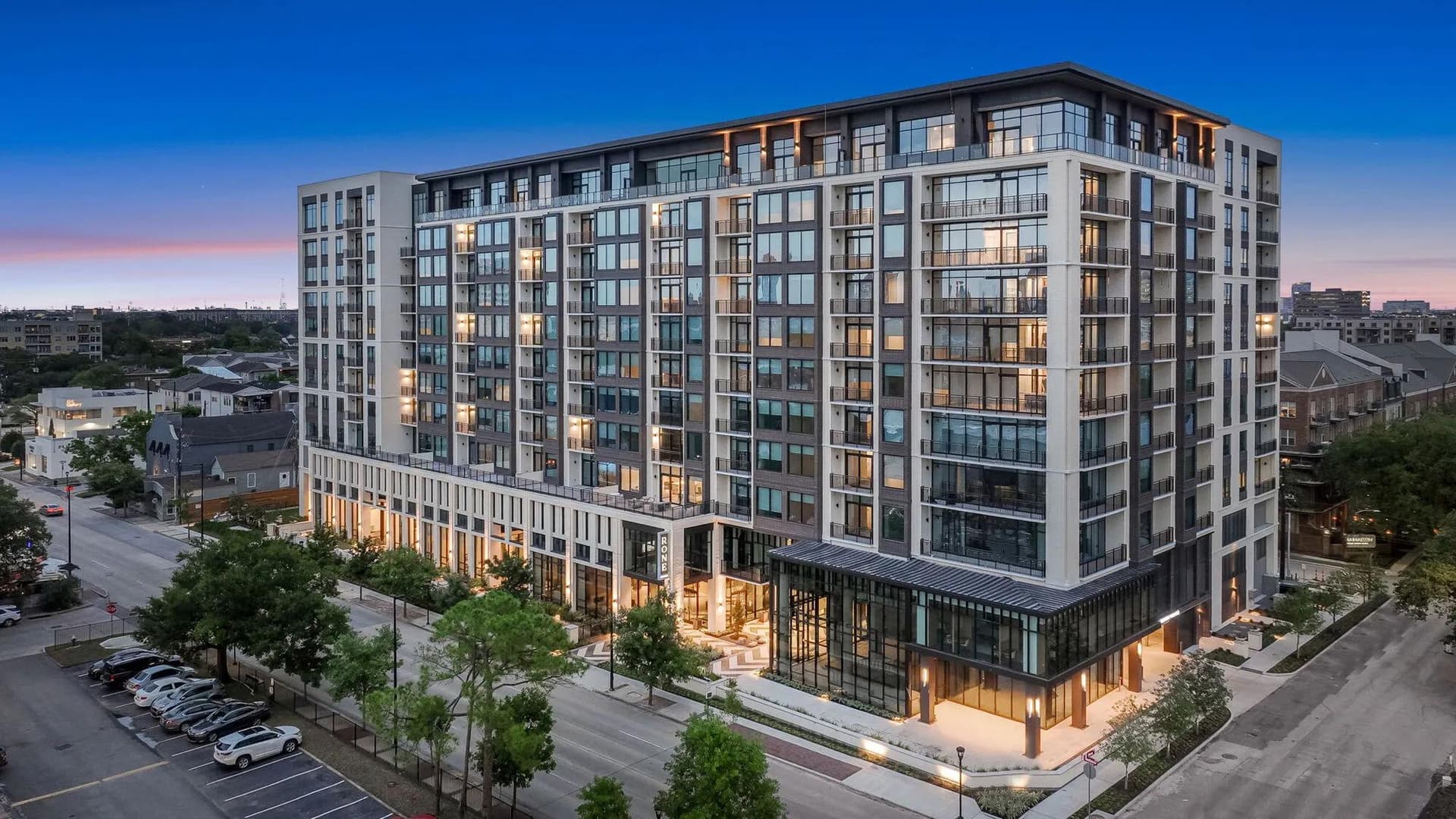 Modern mid-rise apartment community in Houston photographed at dusk with lit leasing lobby and street-level amenity space